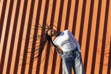 Smiling young woman tossing hair in front of wall - LMCF00869