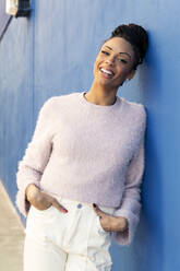 Happy young woman leaning on blue wall - LMCF00890