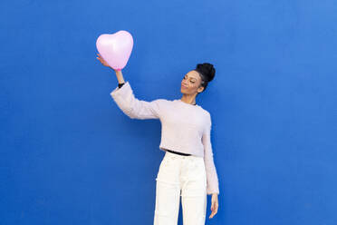 Smiling young woman standing with pink heart shaped balloon - LMCF00909