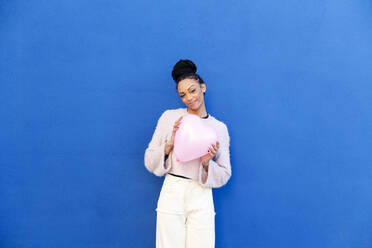 Happy young woman standing with pink heart shaped balloon - LMCF00910