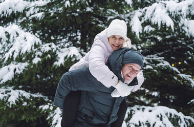 Glücklicher Mann nimmt Frau vor schneebedeckten Bäumen huckepack - OLRF00168
