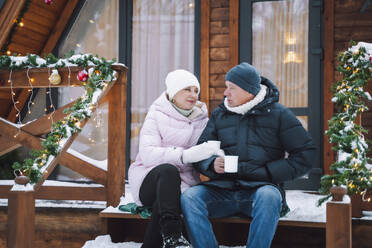 Mature couple having tea sitting on porch of log cabin - OLRF00173