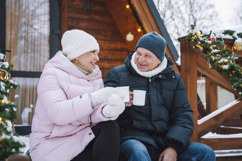 Glückliches reifes Paar genießt heißen Tee auf der Veranda in der Nähe der Blockhütte - OLRF00175