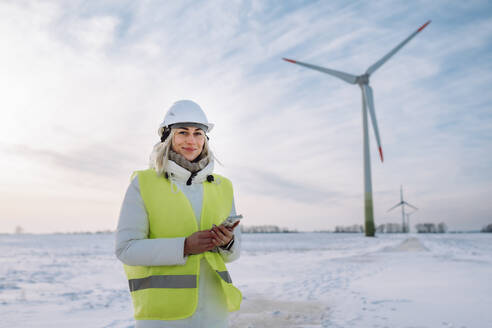 Lächelnde Frau mit Handy in der Hand vor einem Windpark - OLRF00186