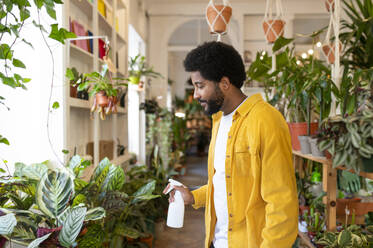 Botanist spraying water on plants at shop - VRAF00392