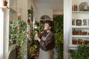 Botanist spraying water on plant hanging in store - VRAF00401