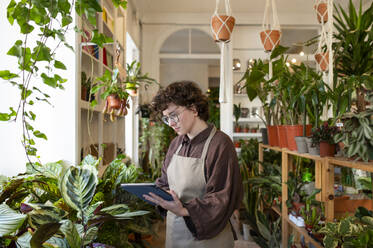 Botaniker mit Tablet-PC inmitten von Pflanzen in einer Gärtnerei - VRAF00402