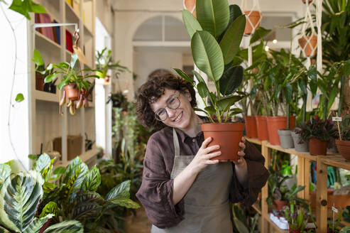 Happy shop owner holding potted plant at nursery - VRAF00403