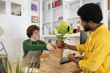 Botanikerin hilft einem Kunden beim Kauf einer Pflanze in einer Gärtnerei - VRAF00422