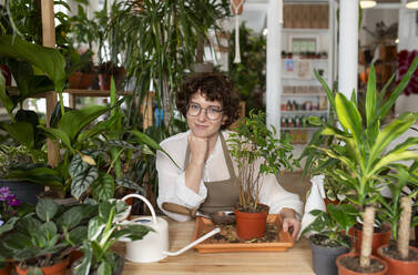 Smiling botanist potting plant at table in shop - VRAF00425