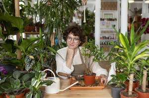 Smiling botanist potting plant at table in shop - VRAF00425