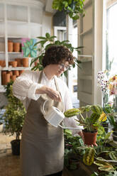 Botanist pouring water in potted plant at nursery - VRAF00431