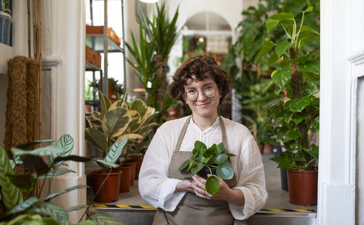 Smiling botanist holding potted plant at nursery - VRAF00437