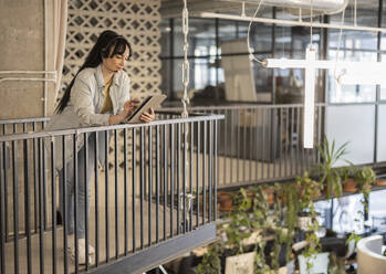 Businesswoman wearing headset using tablet PC leaning on railing at office - JCCMF11174