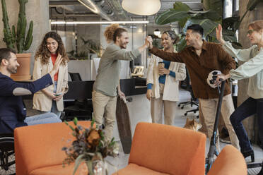 Happy diverse colleagues giving high-five to each other in meeting at office - JCCMF11180