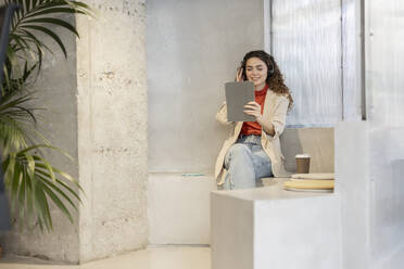 Lächelnde junge Geschäftsfrau, die am Arbeitsplatz sitzend mit einem Tablet-PC Musik hört - JCCMF11195