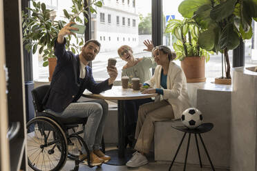 Businessman in wheelchair taking selfie with colleagues sitting at table - JCCMF11200