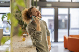 Glücklicher Geschäftsmann, der sich im Büro über sein Mobiltelefon unterhält - JCCMF11226