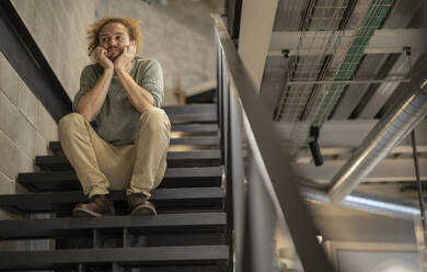 Upset businessman sitting on staircase at office - JCCMF11228