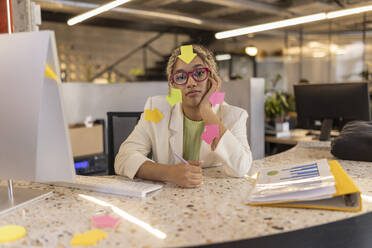 Überarbeitete Geschäftsfrau mit Pfeil-Klebezetteln überall auf ihr sitzend im Büro - JCCMF11248