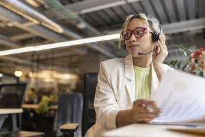 Junge Geschäftsfrau, die über ein Headset spricht und am Schreibtisch im Büro sitzt - JCCMF11249