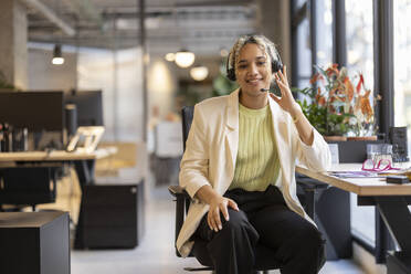 Lächelnde Geschäftsfrau mit Headset sitzt am Schreibtisch im Büro - JCCMF11250