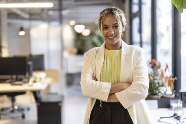 Smiling young businesswoman standing with arms crossed at office - JCCMF11251