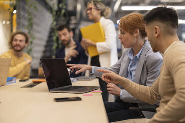 Businessman and businesswoman pointing at laptop in office - JCCMF11256