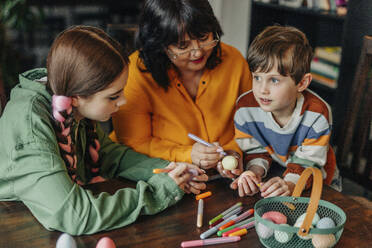 Glückliche Großmutter mit Enkelkindern beim Bemalen von Ostereiern - VSNF01585