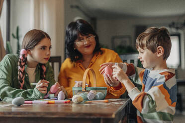 Family decorating Easter eggs at table - VSNF01591