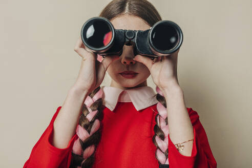 Young woman looking through binocular in front of wall - VSNF01625