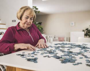 Ältere Frau spielt ein Puzzlespiel am Tisch - UUF31155