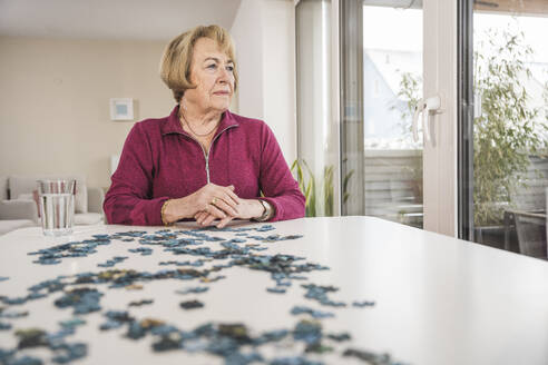 Nachdenkliche Frau sitzt mit Puzzle am Tisch - UUF31157