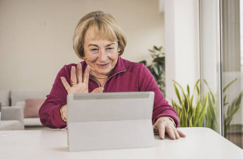 Happy senior woman waving on video call through tablet PC - UUF31160