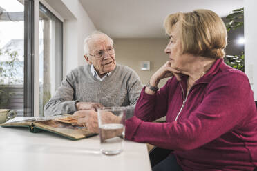 Älterer Mann und Frau sitzen mit Fotoalbum am Tisch - UUF31164