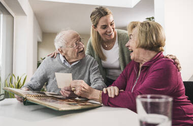 Happy home caregiver with senior couple holding photograph - UUF31168