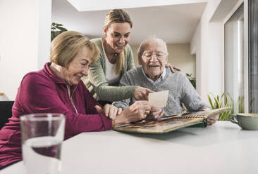 Happy home caregiver with senior couple looking at photograph - UUF31169