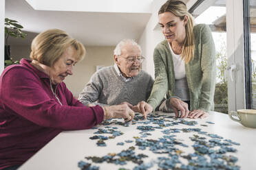 Hauspflegerin mit älterem Ehepaar beim Puzzeln am Tisch - UUF31170