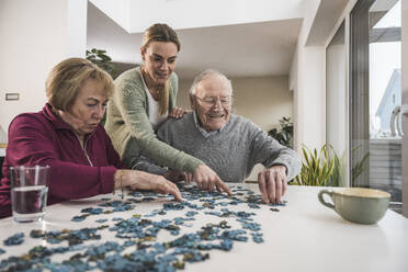 Glückliche Betreuerin zu Hause, die mit einem älteren Paar ein Puzzlespiel spielt - UUF31171