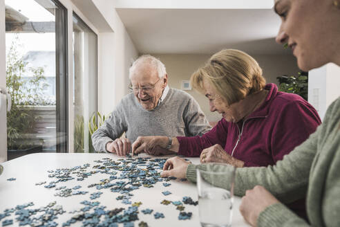 Hauspflegerin spielt Puzzle-Spiel mit glücklichem Seniorenpaar - UUF31172