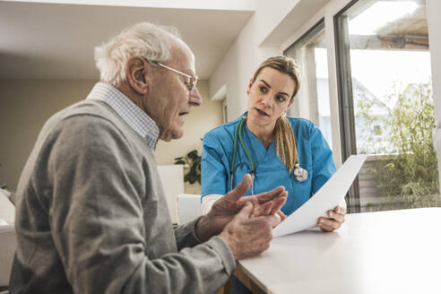 Home caregiver discussing over medical report with man - UUF31181