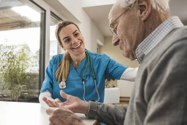 Lächelnde Krankenschwester misst den Puls eines älteren Mannes, der am Tisch sitzt - UUF31182