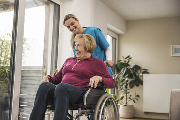Glückliche häusliche Pflegerin kümmert sich um eine ältere Frau, die im Rollstuhl sitzt - UUF31186
