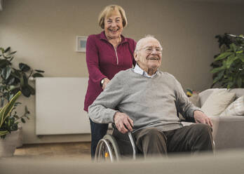 Glückliche Frau mit Mann, der zu Hause im Rollstuhl sitzt - UUF31190