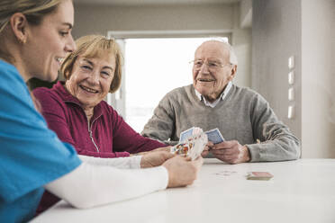 Glückliche Hauspflegerin spielt Karten mit einem älteren Paar - UUF31193