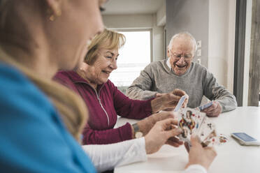 Smiling home caregiver playing cards with senior couple - UUF31194