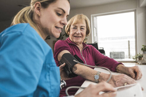 Smiling home caregiver examining blood pressure of woman with machine - UUF31202