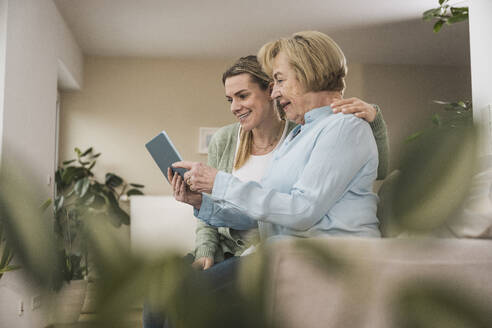 Lächelnde Hauspflegerin mit älterer Frau, die einen Tablet-PC benutzt - UUF31205
