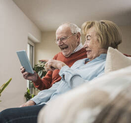 Glückliches älteres Paar, das einen Tablet-PC im heimischen Wohnzimmer benutzt - UUF31209