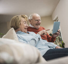 Fröhliches älteres Ehepaar bei der Nutzung eines Tablet-PCs im heimischen Wohnzimmer - UUF31210